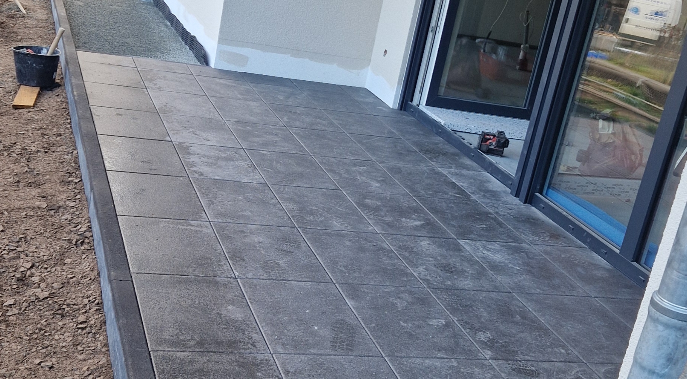 Eine graue gepflasterte Terrasse an einem modernen Gebäude mit Glasschiebetüren.